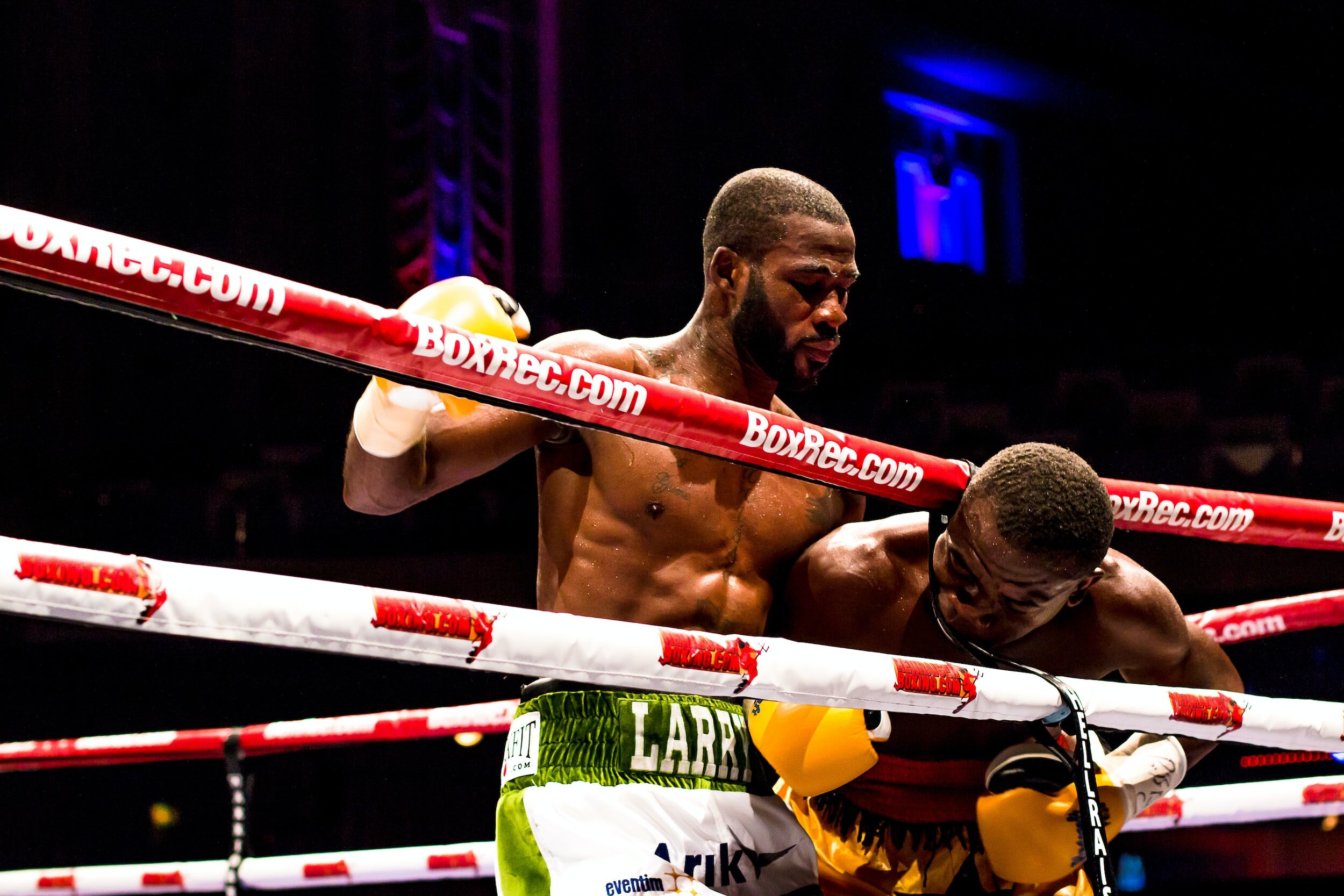 Two men engaged in a boxing match, one with his head between the ropes.