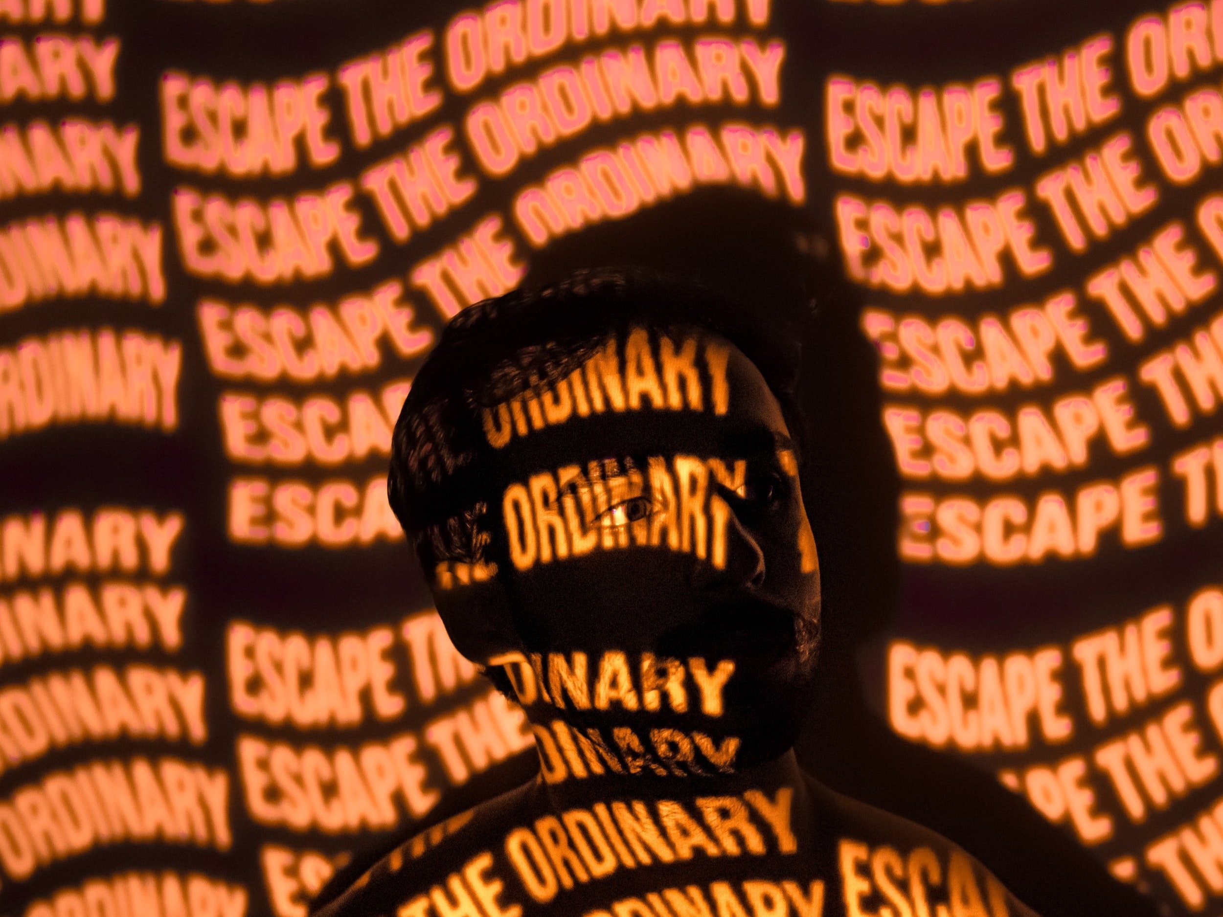 a man in the dark with the words "Escape the Ordinary" projected onto him and the wall