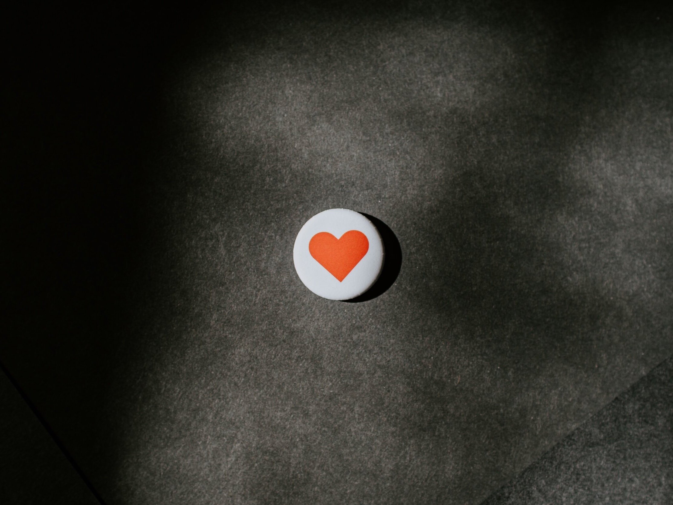 On a felt surface, a white badge with a single red love heart is displayed.