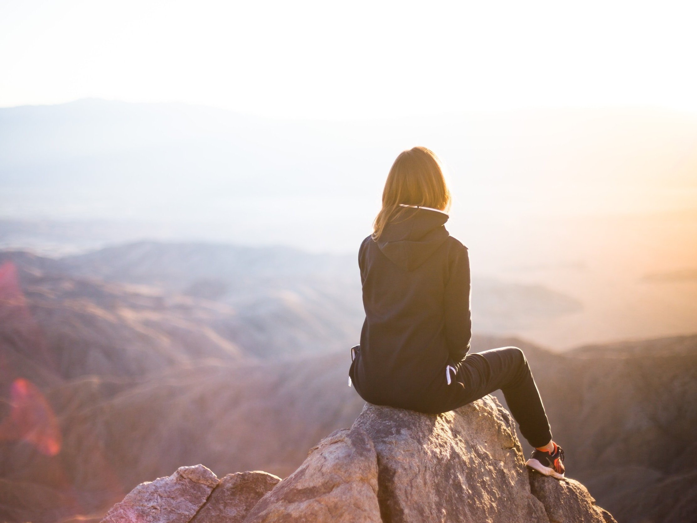 A lady sits on a mountain top, taking in the breathtaking scenery.