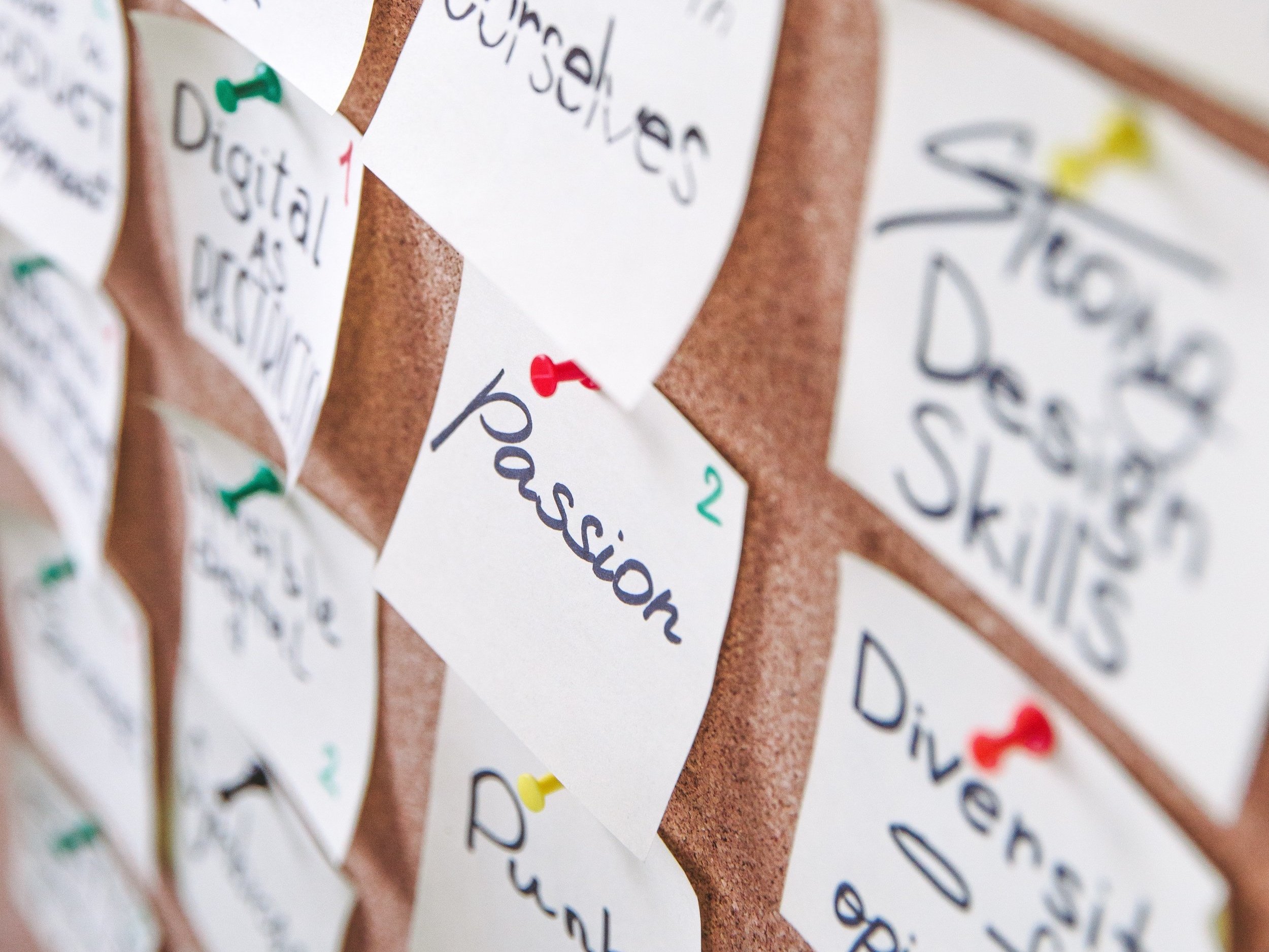 There are numerous sticky notes with various messages on a cork board, but the one with the word "Passion" stands out.