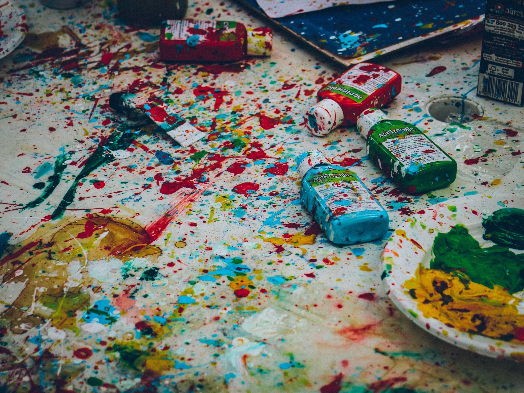 A messy surface with paint-covered paint bottles and paint splattered everywhere.