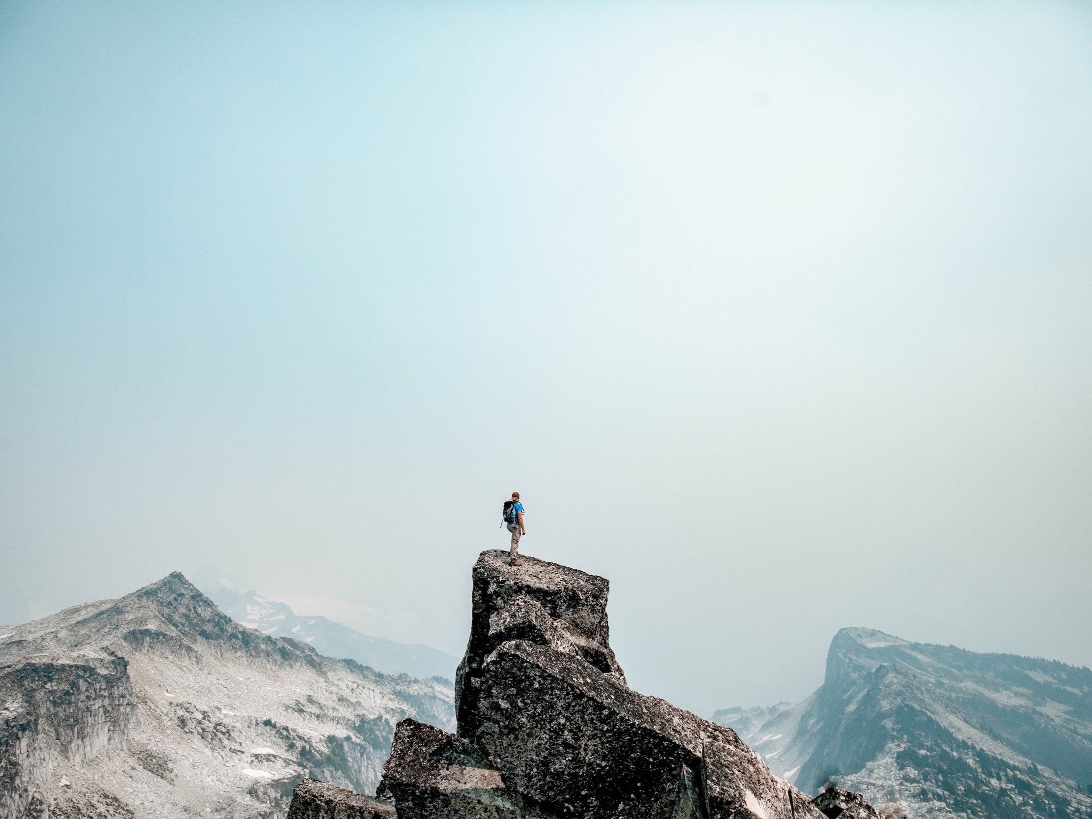 A man ascends to the peak of a mountain and looks out across the other mountains.
