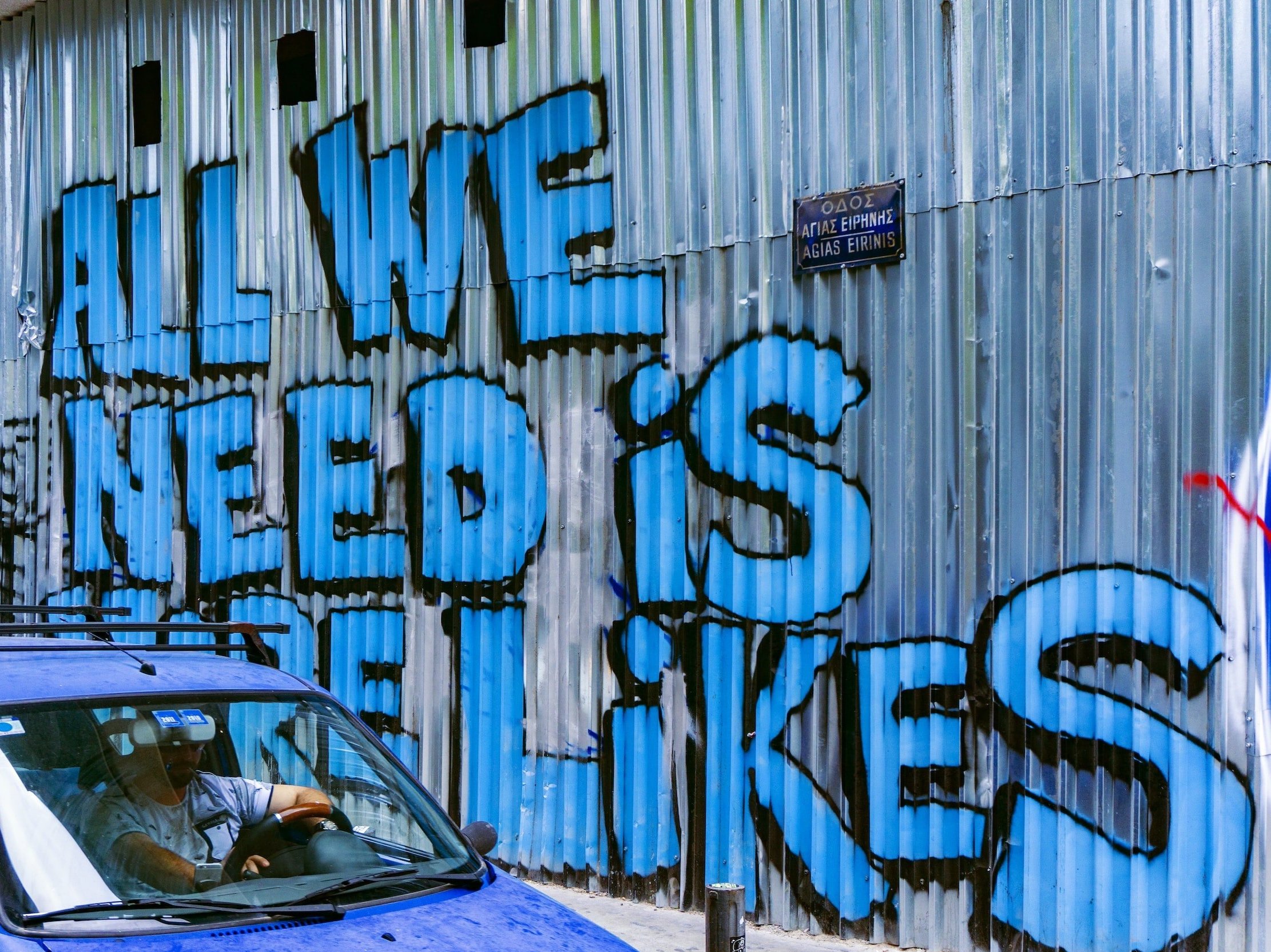 Graffiti with the words "All We Need Is More Likes" sprayed on a corrugated iron wall.