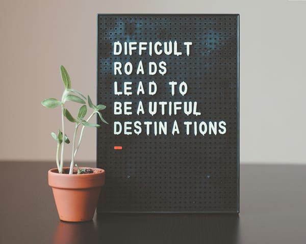 Message board saying "Difficult roads lead to beautiful destinations" next to a potted plant, symbolising growth.