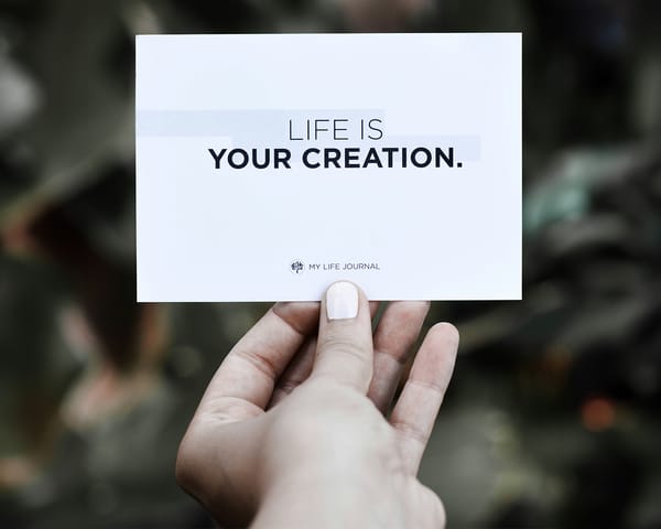 Hand holding a card with "LIFE IS YOUR CREATION." text, symbolising personal and professional self-determination.