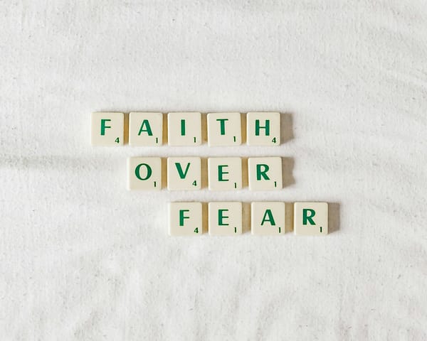 Scrabble tiles on a white surface spell "FAITH OVER FEAR."