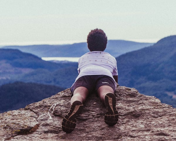 Person lying on a mountain top, overlooking a vast landscape, symbolising contemplation.