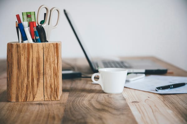 A wooden desk with a pen holder, coffee cup, and laptop is perfect for considerations before starting a freelance business.