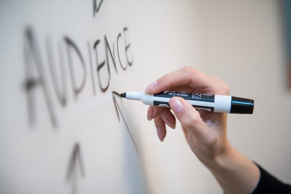 Close-up of a hand writing the word 'AUDIENCE' with a marker on a whiteboard.