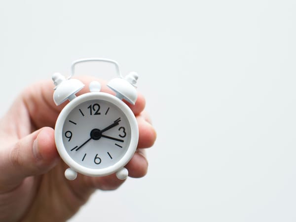 Hand holding white alarm clock, symbolising Pomodoro time management method.
