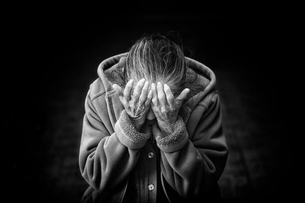 Elderly woman covering her face with hands, expressing sorrow or regret, in a black and white photo.