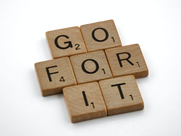 Scrabble tiles arranged to spell "GO FOR IT" on a white background, symbolising motivation and action.