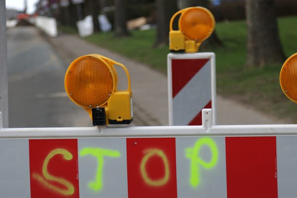 Road barrier with yellow lights and a spray-painted "STOP" sign, signaling caution.