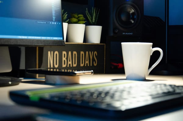 Workspace with a computer, speaker, coffee mug, and a sign that reads "NO BAD DAYS."