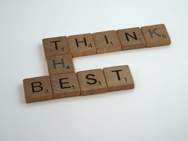 Scrabble tiles on a white surface spell "THINK BEST," emphasising positive thinking.