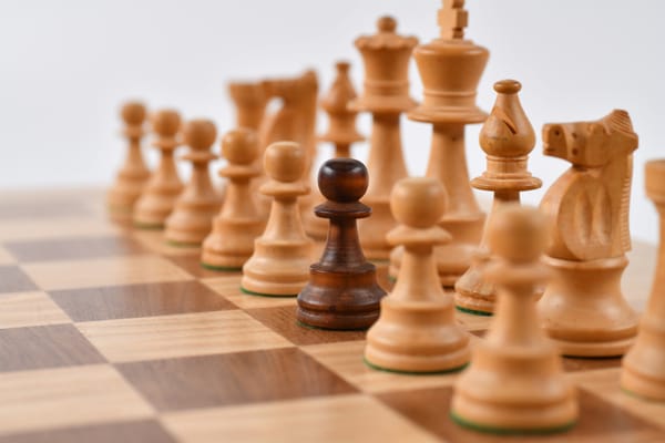 A dark pawn stands out among lighter chess pieces on a board.