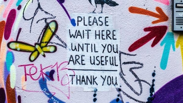 "Wait until useful" graffiti with butterflies amid colours critiques societal productivity pressures.