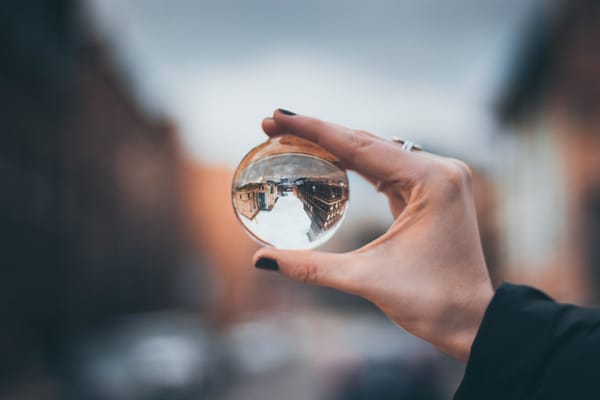 Hand holding crystal ball with inverted city view - need for diverse perspectives for greater understanding.