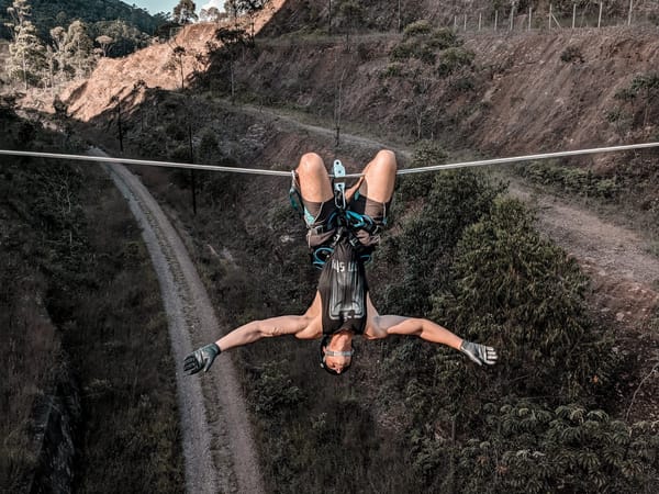 A person ziplining through a lush forest landscape, suspended upside down with arms outstretched and legs crossed.