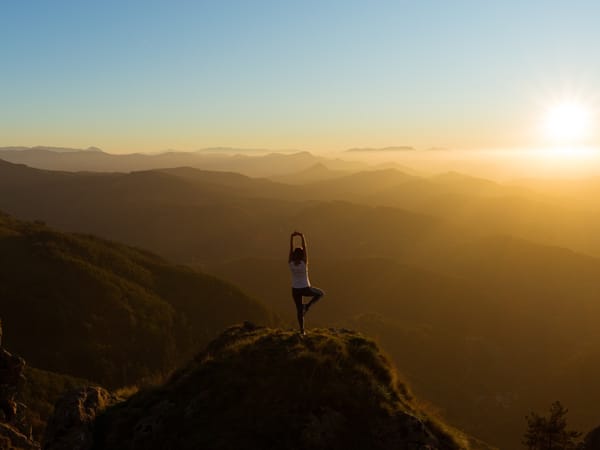 Yoga pose silhouette on rocky outcrop at sunrise over mountains - inner versus outer change metaphor.