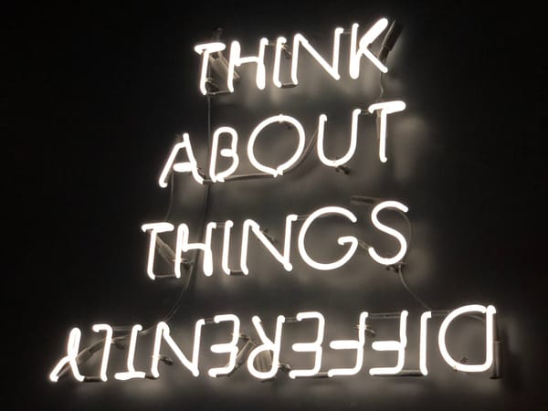 Neon sign: "Think about things differently", implying novel perspectives, not just more effort, drive breakthroughs.